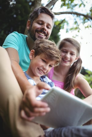 Happy father and kids using digital tablet in garden