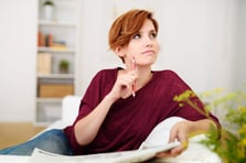 Thoughtful Attractive Young Woman Answering Crossword Puzzle Game on Newspaper at the Living Room Couch.-1